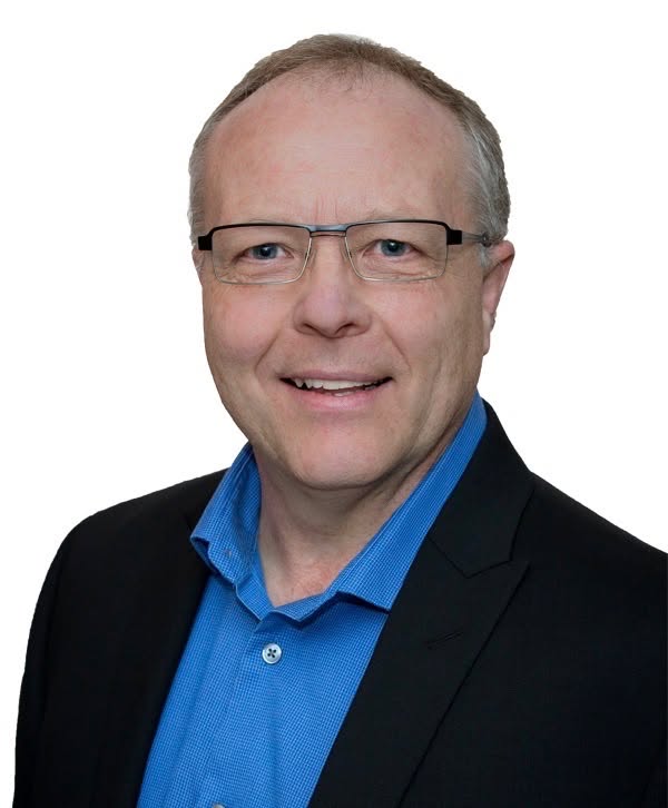 Portrait of Rob Davies smiling, wearing glasses, a blue shirt and a dark blazer